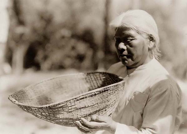 Miwok woman holding sifting basket, California.
