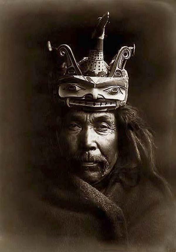 Kwakiutl man, head-and-shoulders portrait, facing front,  wearing a mask depicting a loon on top of a man's head to facilitate the loon changing into the form of a man.