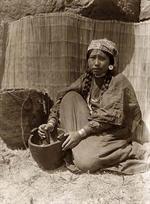 Tlakluit woman seated with mortar and pestle.