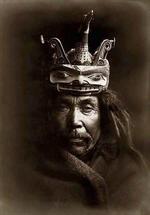 Kwakiutl man, head-and-shoulders portrait, facing front,  wearing a mask depicting a loon on top of a man's head to facilitate the loon changing into the form of a man.